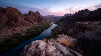 Obraz premium A winding river carves through a rugged desert canyon at twilight with soft colors painting the sky and illuminated rock formations
