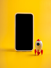 Minimal concept of digital startup and mobile marketing with blank smartphone screen and toy rocket...
