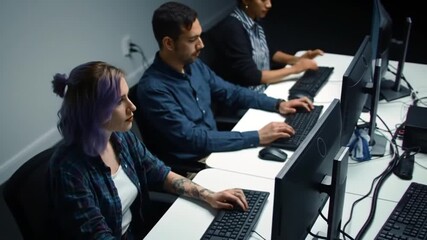 Three diverse individuals are diligently working on computers in a modern office or classroom setting, focused on their tasks. - Powered by Adobe