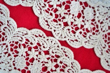 Curved scalloped lace aligned diagonally on red background, revealing twin gaps for a graceful and artistic textile composition