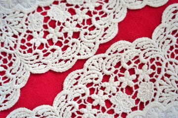 Curved scalloped lace patterns aligned with twin gaps of red background, creating a symmetrical and elegant textile layout