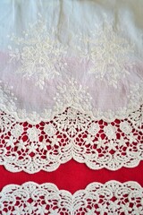 Embroidered floral fabric with curved scalloped lace trim on red background, showcasing romantic elegance and vintage textile artistry
