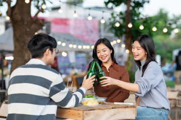 Asian woman and man friend clinking drink bottles while sitting at table in a campground restaurant.