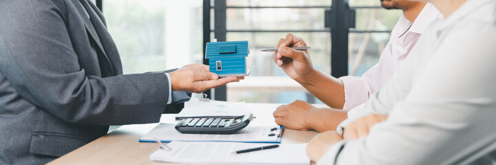 Mortgage consultation panorama with miniature house model in hand, financial advisor meeting clients, property investment, home loan agreement, real estate planning and housing business negotiation.