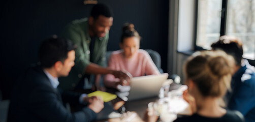 Group of diverse professionals collaborating around a laptop in a meeting, sharing ideas and teamwork in a bright modern office that fosters creativity and productivity.