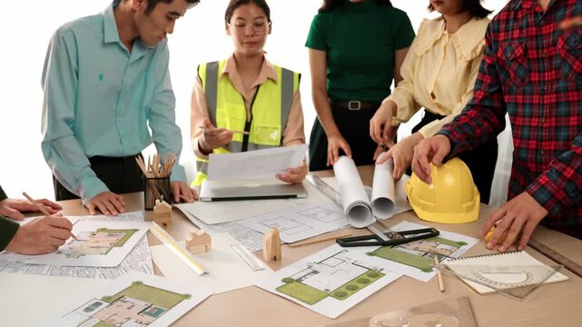 Smart architect and safety engineer discussion about building blueprint on table with architectural document, measurement tools and wooden block scatter around at modern office. Closeup. Delineation.