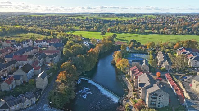 Ascending drone shot over Wetherby town in West Yorkshire, showing the winding River Wharfe, bordering Wetherby Ings parkland, surrounding houses and lush countryside.