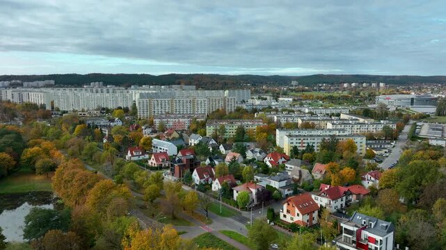 Aerial drone view of a European city suburb in autumn. A mix of single-family homes, small apartment buildings, and large communist-era housing blocks.