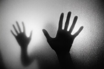 Shadowy hands pressed against a misty glass surface, creating a suspenseful atmosphere