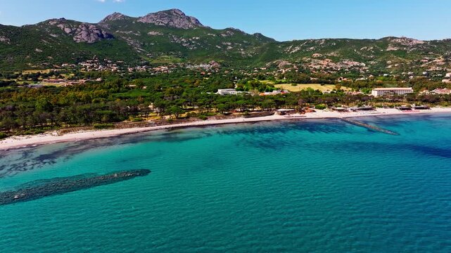 Aerial drone shot over the beach in Corsica. High view of green mountains and the turquoise sea. Summer holidays destination.