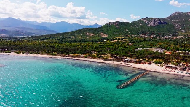 Aerial drone shot over the beach in Corsica. High view of green mountains and the turquoise sea. Summer holidays destination.