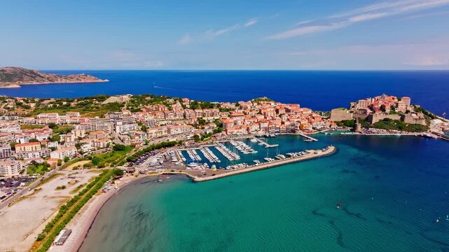 Aerial drone shot over the coastal town of Calvi in Corsica. View of the citadel fortress overlooking the city. Summer holidays destination. Bright blue sky, vibrant turquoise sea.