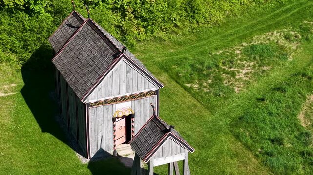 Overhead aerial of reconstructed Viking church and outbuilding in green grassy field at Moesgaard, Aarhus, Denmark, with visible path outlines and sunlit roofs