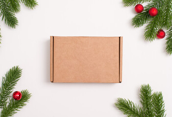 Closed kraft gift box mock-up on white background decorated with fir branches and red mini balls. Perfect for Christmas packaging design, product branding, or festive flat lay concepts.