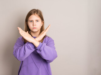 Serious preteen girl in purple outfit showing “no” gesture with arms crossed on grey background. Perfect for refusal, rejection, prohibition, or disagreement concepts.