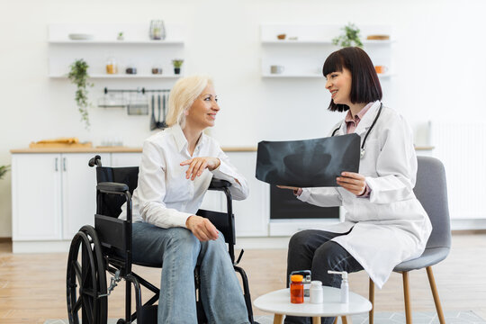 A female doctor shows an X-ray to an elderly patient in a wheelchair, discussing the results in a bright room. The patient smiles, indicating a positive interaction.
