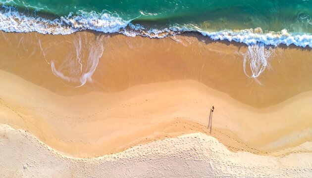 Aerial view turquoise waves meeting a sandy beach, footprints and one figure walking along the shore