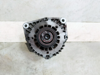Old broken car alternator after changing on concrete floor. Old dirty car generator on gray background. Cracked and old rusty used alternator for car. Auto part, engine parts, maintenance concept.