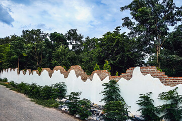 Decorative curved fence wall. Beautiful stuccoed brick wall features unique and attractive design, characterized by uneven, varying height levels. rendered brick wall design non uniform wall heights.