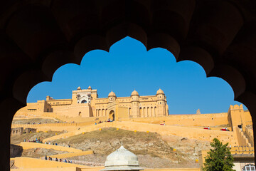 Captured in Jaipur, India &mdash; a stunning view of the historic Amber Fort framed through a traditional arch, showcasing the golden sandstone walls and majestic Rajput architecture under a clear blue sky.