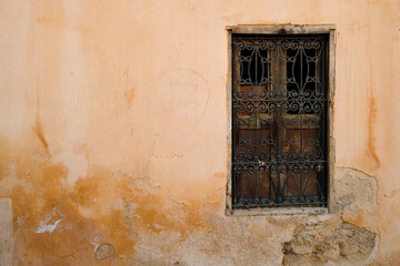 Ornamented wooden window on aged yellow clay wall in Fes, Morocco, showcasing historic Islamic craftsmanship and weathered textures.