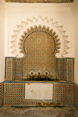 Old Moroccan wall fountain in Tangier decorated with brown-orange tiles and Islamic geometric patterns.