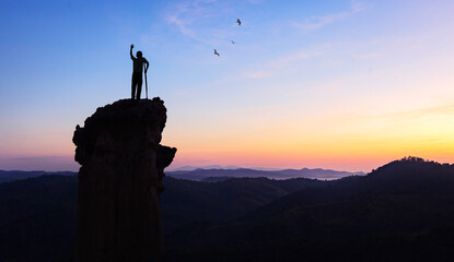 Silhouette a disabled man standing up and raising his hand at  sunrise background