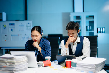Asian business colleagues feeling stress and fatigue from workload, working late under deadline pressure and tension in modern office.