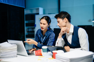 Asian business colleagues feeling stress and fatigue from workload, working late under deadline pressure and tension in modern office.