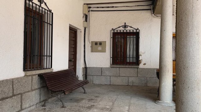 Slow-motion ascending shot of a traditional Castilian portico in Plaza Mayor, La Puebla de Montalb&aacute;n, Toledo. Wooden beams, stone columns, white plaster walls, and iron grilles under autumn sunlight.