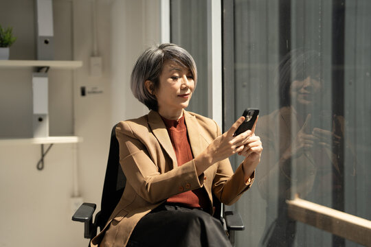 Asian businesswoman CEO   using smartphone application in modern office. Mature adult professional business woman using mobile phone cellphone.