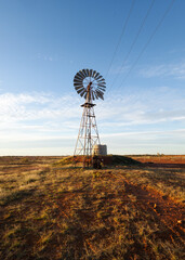 A wind powered water pump using borehole water to fill a water tank in the semi-arid outback with clouds and blue sky in the background at Thargomindah in South Western Queensland, Australia. © Shirley and Johan