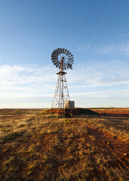 A wind powered water pump using borehole water to fill a water tank in the semi-arid outback with clouds and blue sky in the background at Thargomindah in South Western Queensland, Australia.