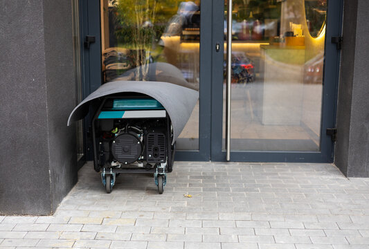 Electric generator stands on a street and supplies electricity to a shop or cafe during blackout. Concept of backup power supply and blackout