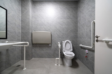 An accessible bathroom with grab bars, large windows, and gray tiles.