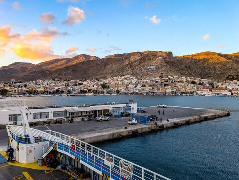 Large ferry boat approaching the Pothia port, Kalymnos island, Greece, with waterfront buildings and mountains glowing in the warm sunset light