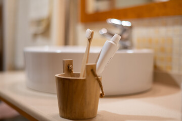 Bamboo toothbrush and white tube of toothpaste standing in a wooden holder on a bathroom counter, representing ecological alternatives and daily health care practices