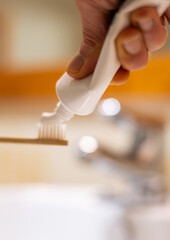 Hand applies toothpaste onto a natural bamboo toothbrush in a bright bathroom setting, emphasizing sustainable dental care, daily oral hygiene routine, and environmental consciousness