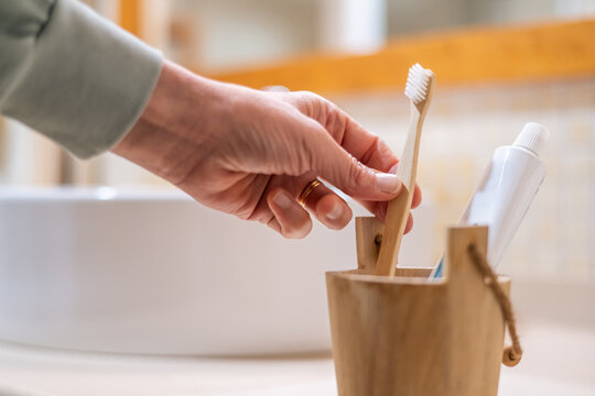 Hand selecting a bamboo toothbrush from a natural wooden holder in a bright bathroom, showcasing sustainable living and eco-friendly oral hygiene practices for daily dental care