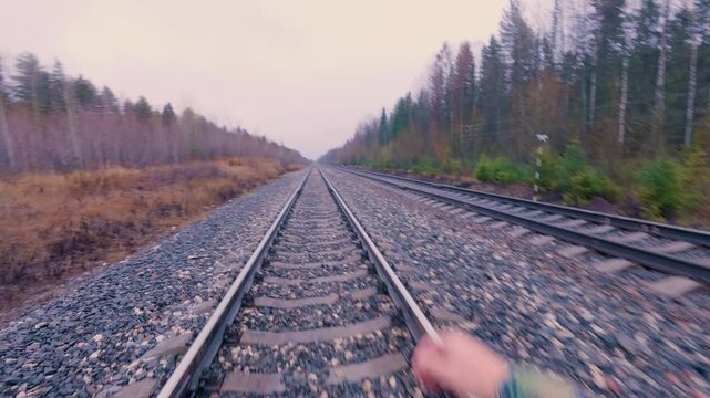 A man walks along a double-track railway. A walk along the rails and sleepers. Railway tracks. From the first person.