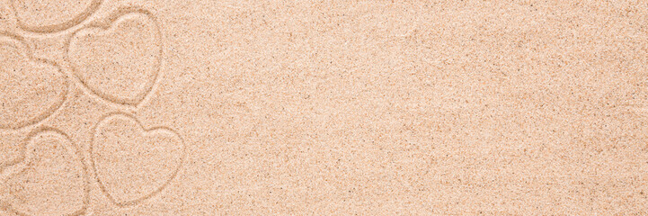 Heart shape prints on dry light brown sea sand background. Closeup. Love concept. Closeup. Wide banner. Empty place for text. Top down view.