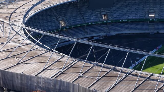 Detailed aerial image of modern stadium stands with empty white seats, stairways, steel roof trusses, and a blank scoreboard at Kaunas Sports Stadium.