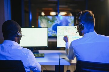 Happy Confident Technical Customer Support Specialist Having a Headset Call in a Monitoring and Control Room Filled with Colleagues and Display Screens