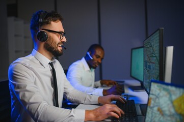 Male Data Scientist Works on Personal Computer Wearing a Headset in Big Infrastructure Control and...
