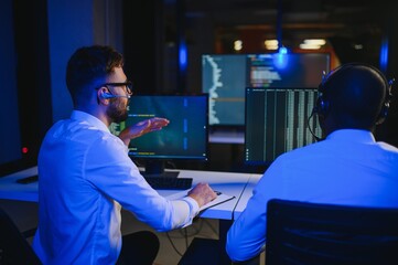 Male Data Scientist Works on Personal Computer Wearing a Headset in Big Infrastructure Control and Monitoring Room