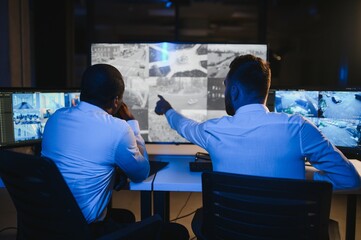 Two male security guards looking at computer screen while one of them explaining detail of video