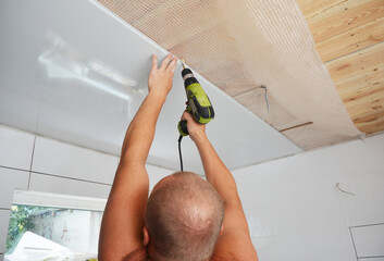 Worker installing plastic ceiling panels with electric drill during renovation