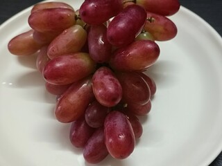 A bunch of fresh red grapes on a white plate, perfect for healthy food concepts, diet menus, natural fruit photography, and nutrition or wellness advertising designs.