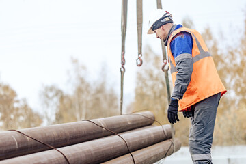 A construction worker in safety gear carefully manages heavy steel pipes at a construction site, showcasing teamwork and industrial work.