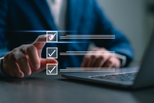 Businessman ticking digital checklist on virtual screen while working on laptop, representing task management, project planning, productivity, and business technology concept. - Powered by Adobe